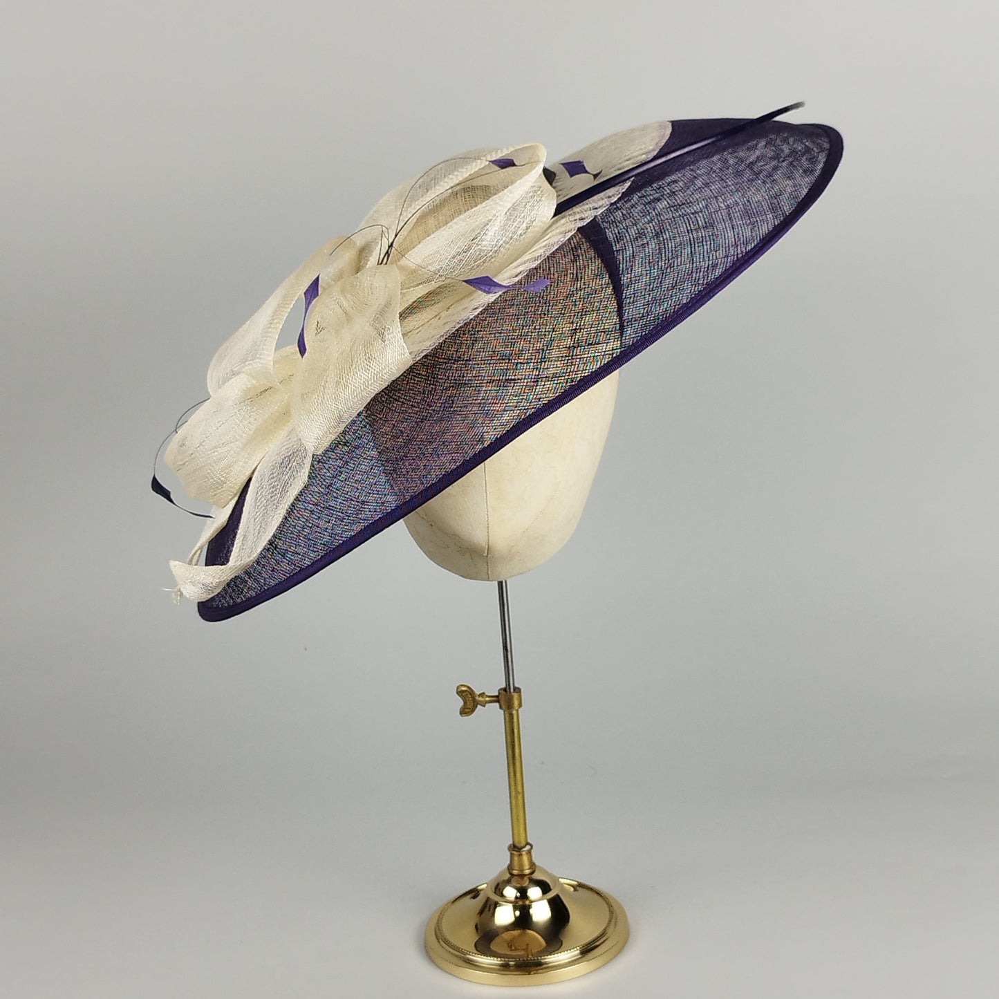 Purple fascinator hat with bow and feather detail, combining vintage style with modern elegance.