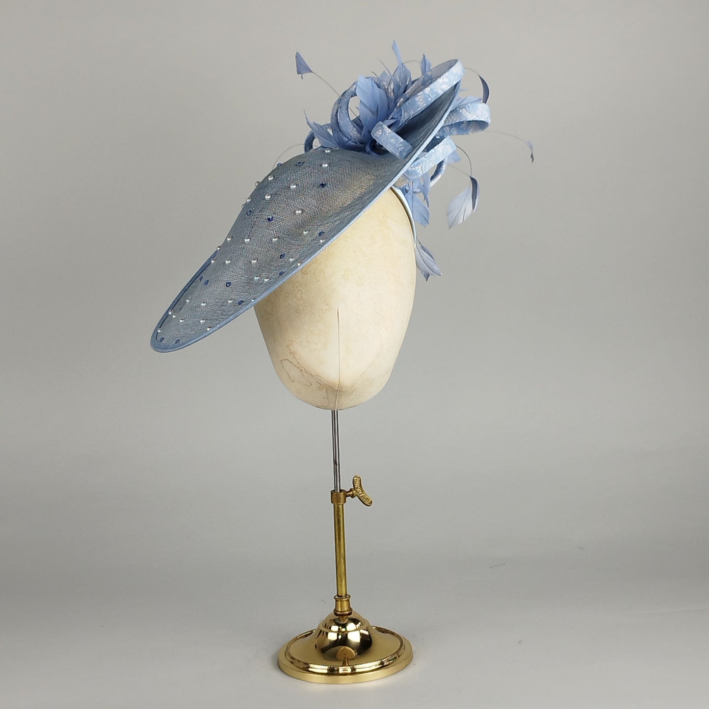 Pale blue hatinator with pearls, crystals, feathers, and bow, perfect for weddings and Royal Ascot. Subtle elegance with a touch of sparkle.