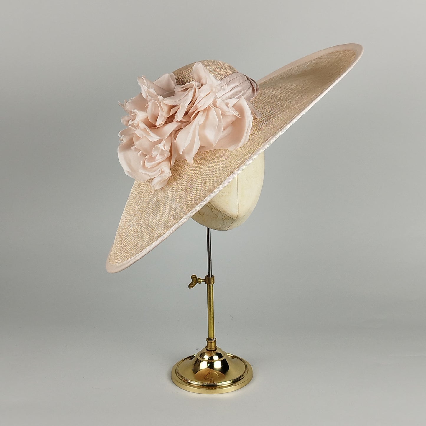 Pale pink wedding hat with silk floral embellishments and silk band. Elegant sloped brim design with subtle apricot undertones. Perfect for brides, mothers of the bride, or guests.