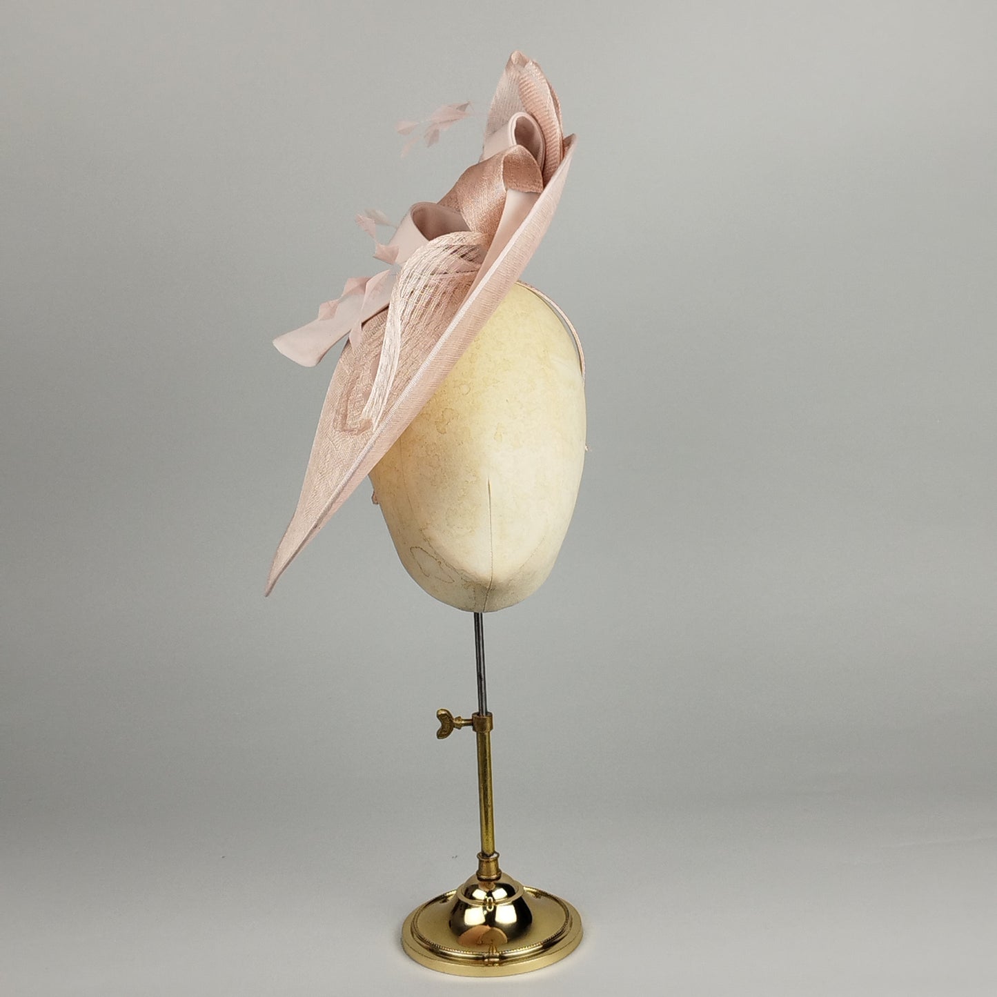 Pale pink hatinator featuring sinamay loops, bows, and feathers. A perfect statement hat for Royal Ascot, weddings, and special occasions. Elegant and playful all in one.