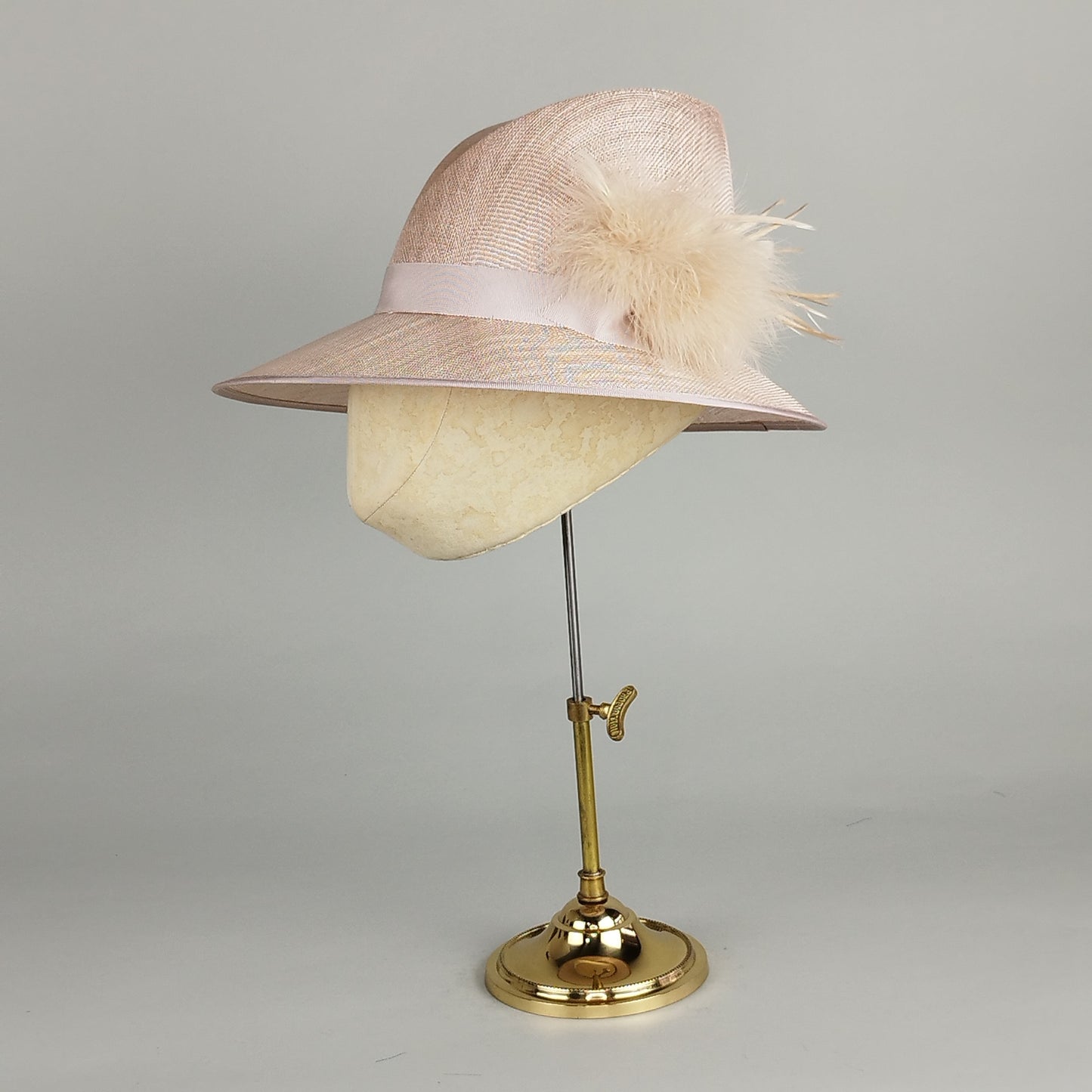 Nude pink trilby-style hat with fluffy side feathers, perfect for weddings, garden parties, or Royal Ascot. Effortlessly chic.