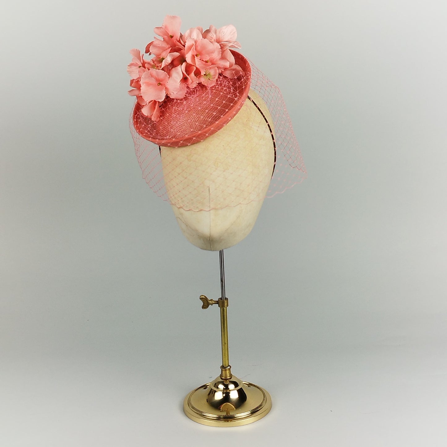 Coral fascinator with pink flowers and birdcage veil, perfect for weddings, Royal Ascot, or race days.