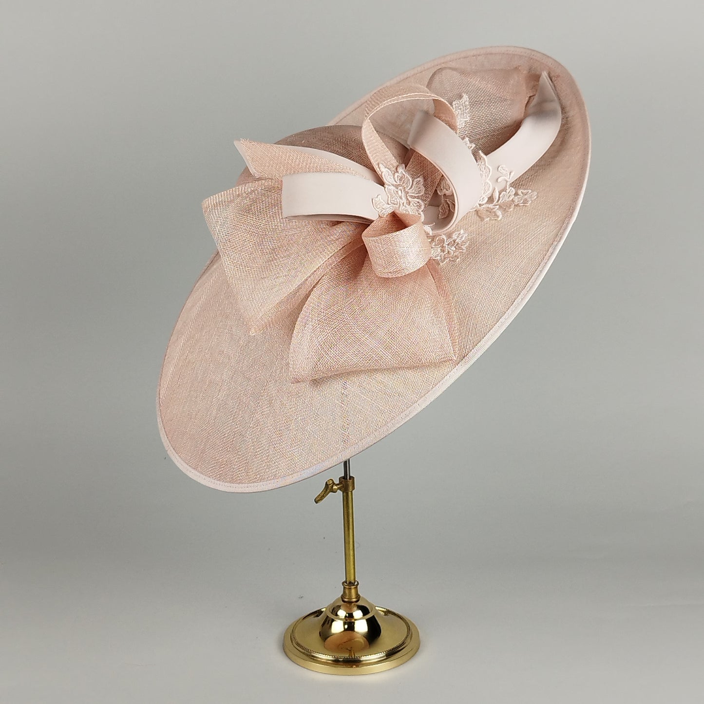 Pale pink wedding hat with sinamay loops, lace overlay, and sloped brim. A perfect choice for the mother of the bride or wedding guests looking for modern elegance.
