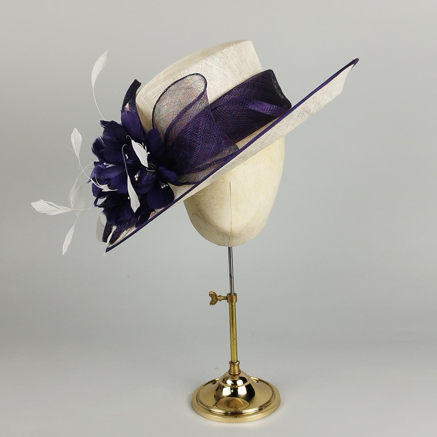 Formal purple and cream feathered wedding hat with a large flower and bow.
