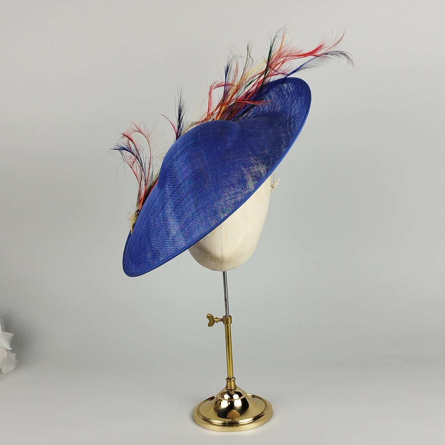 Royal blue hatinator with twirling multicoloured feathers, perfect for weddings and Royal Ascot.