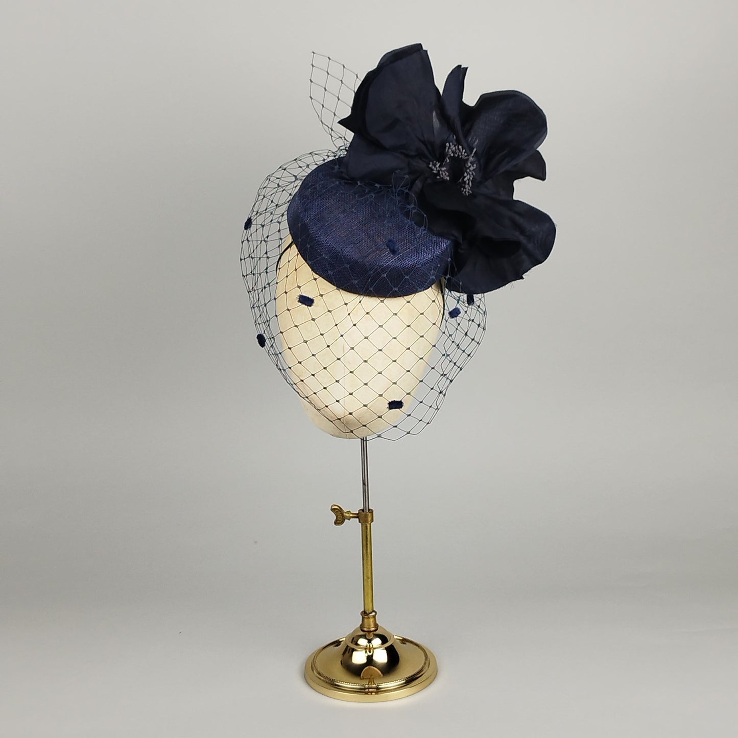 Navy pillbox fascinator with large silk flower, birdcage veil, and vintage dots – bold yet delicate.