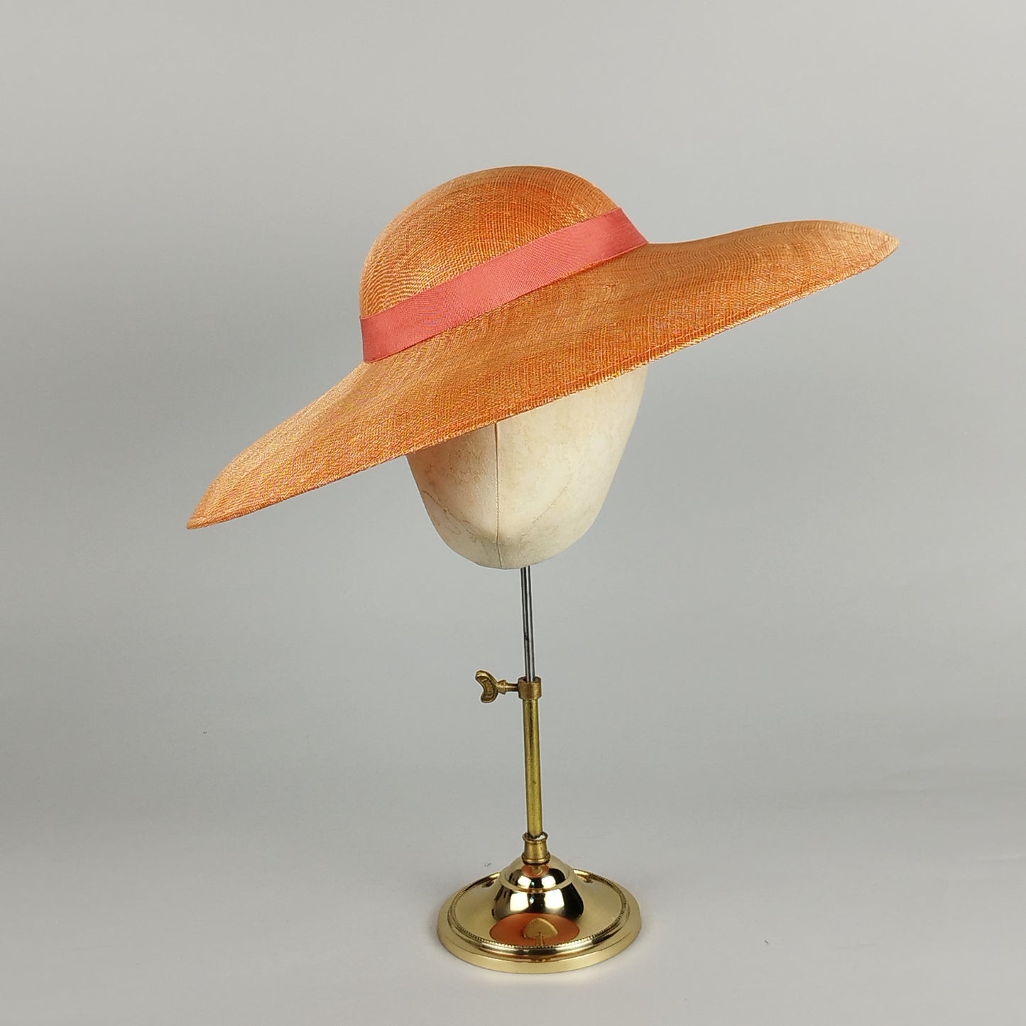 Bold orange hatinator with sweeping brim and peach ribbon – vibrant and elegant.