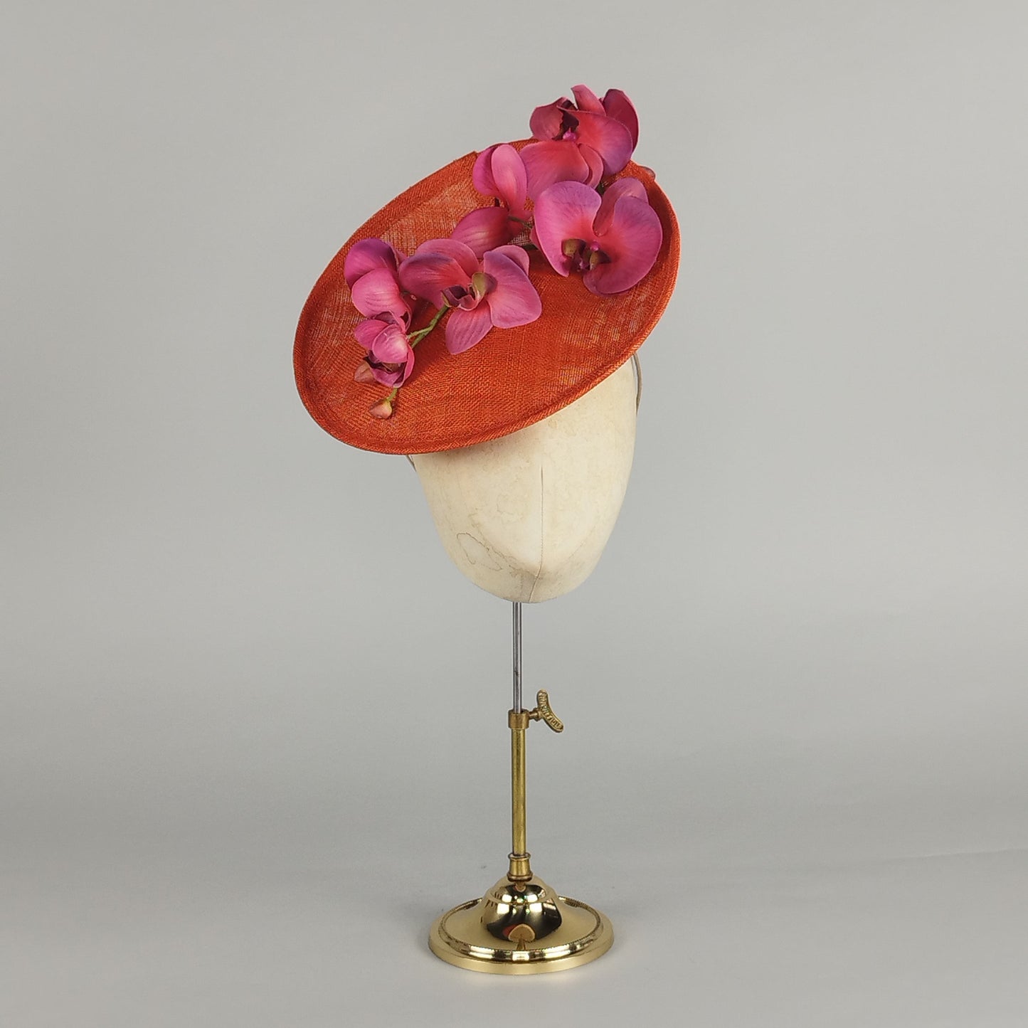 Orange saucer hatinator with cascading fuchsia pink orchids. Perfect for a vibrant wedding or Ascot hat.
