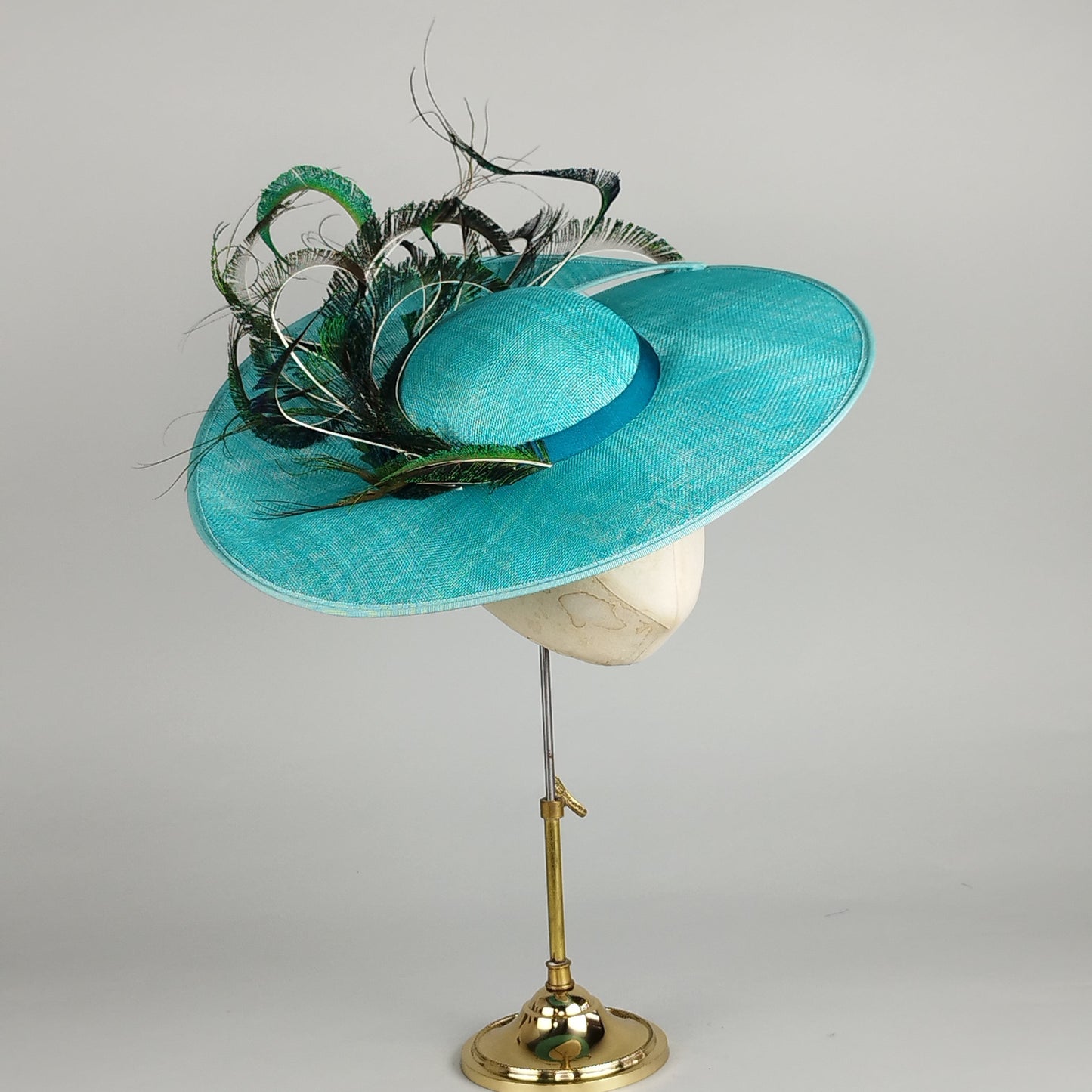 Vibrant turquoise wedding hat with peacock feathers, perfect for making a statement at weddings or Royal Ascot.