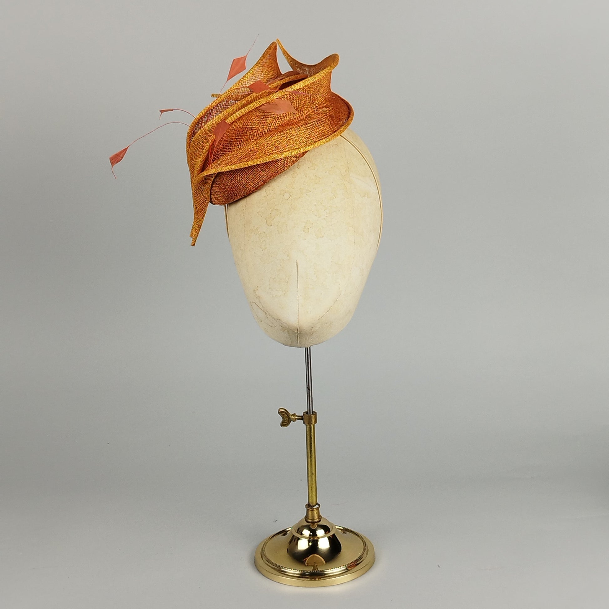 Burnt orange pillbox fascinator with sweeping petals and delicate feathers – playful and elegant.