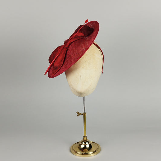Deep crimson sinamay hatinator with silk bow and feather quill, offering refined elegance and structure.