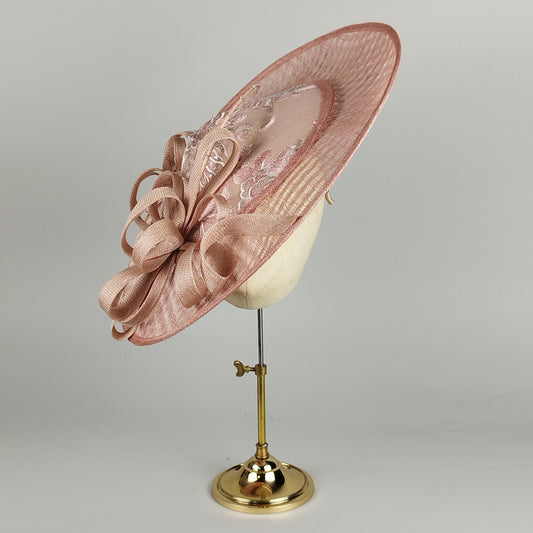 Blush apricot hatinator featuring sinamay loops, lace, curled quill, and crystal beads. An elegant, bold statement piece perfect for Royal Ascot and upscale weddings.