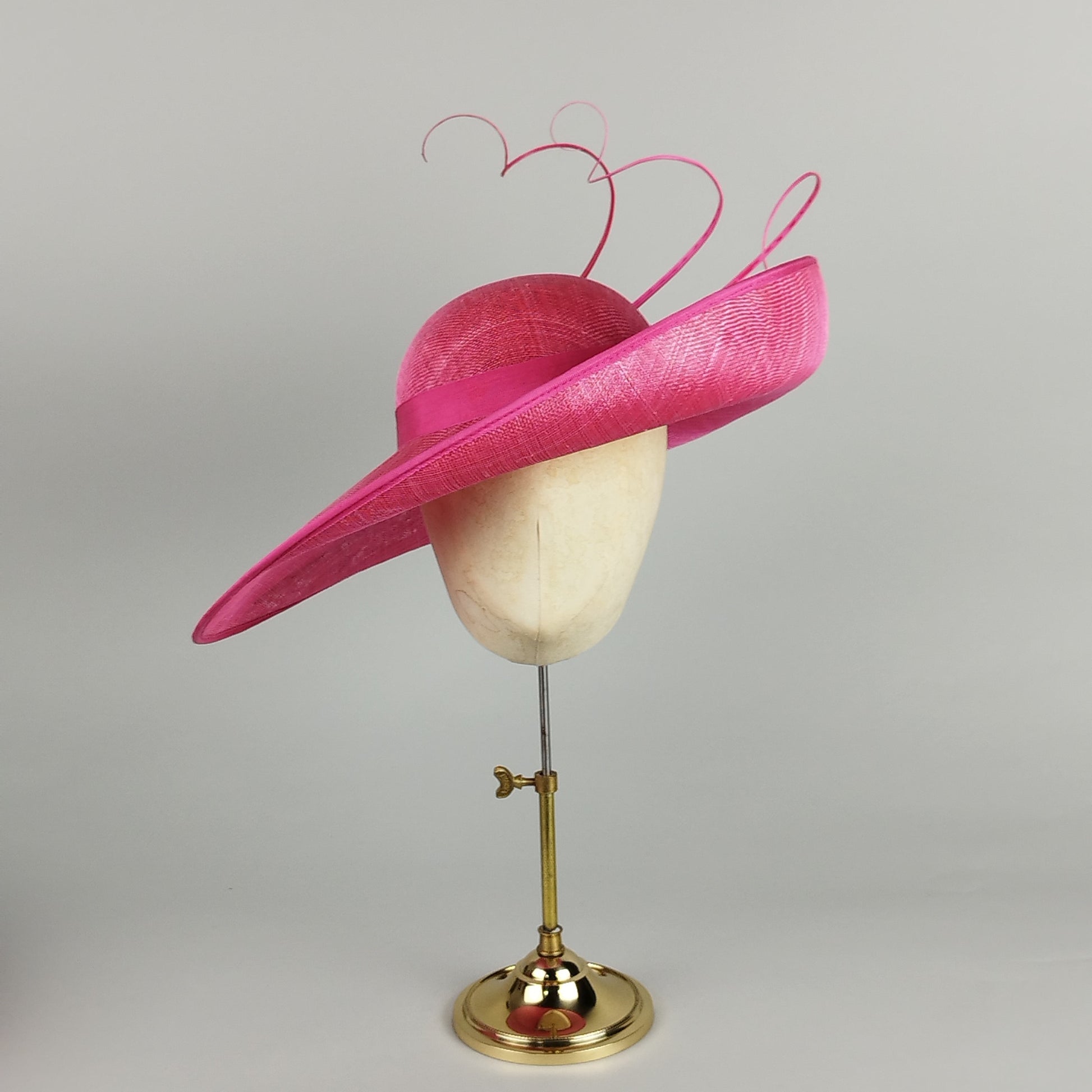Hot pink mother of the bride hat with dramatic upturned brim, deep slope, and three tall, twirled quills.