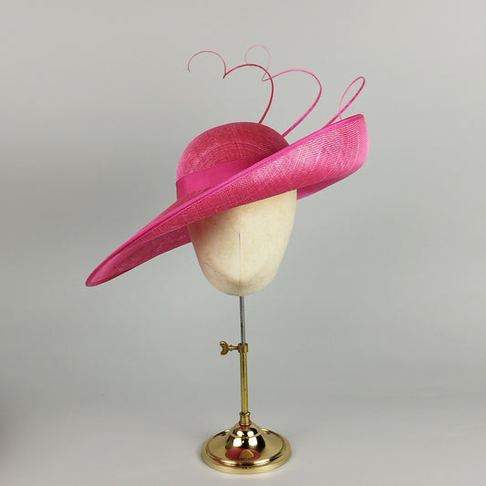 Hot pink mother of the bride hat with dramatic upturned brim, deep slope, and three tall, twirled quills.
