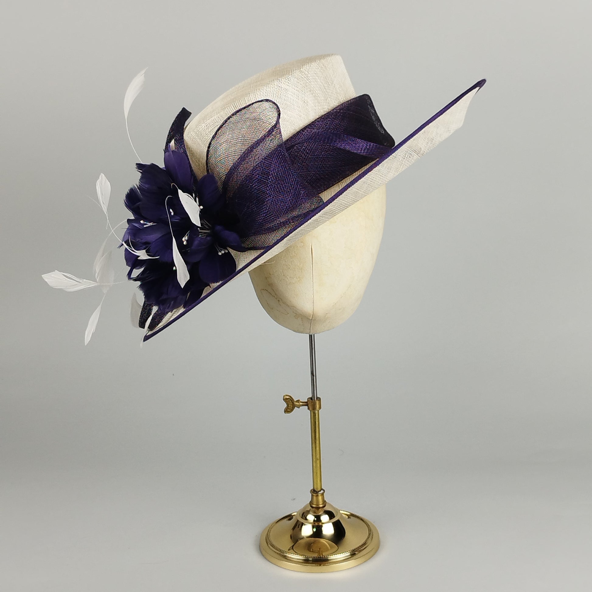 Formal purple and cream feathered wedding hat with a large flower and bow.