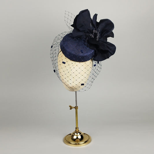 Navy pillbox fascinator with large silk flower, birdcage veil, and vintage dots – bold yet delicate.