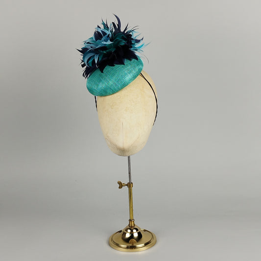 Turquoise pillbox fascinator with large feather flower in blue shades, perfect for weddings and Royal Ascot.