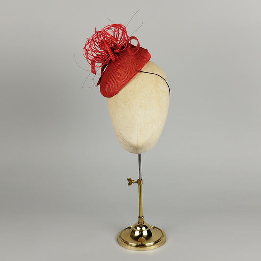 Small red pillbox fascinator with spiky feather flower detail, in fiery red and burnt orange tones. Bold and statement-making with curled, stripped feathers, perfect for making a fashion statement.