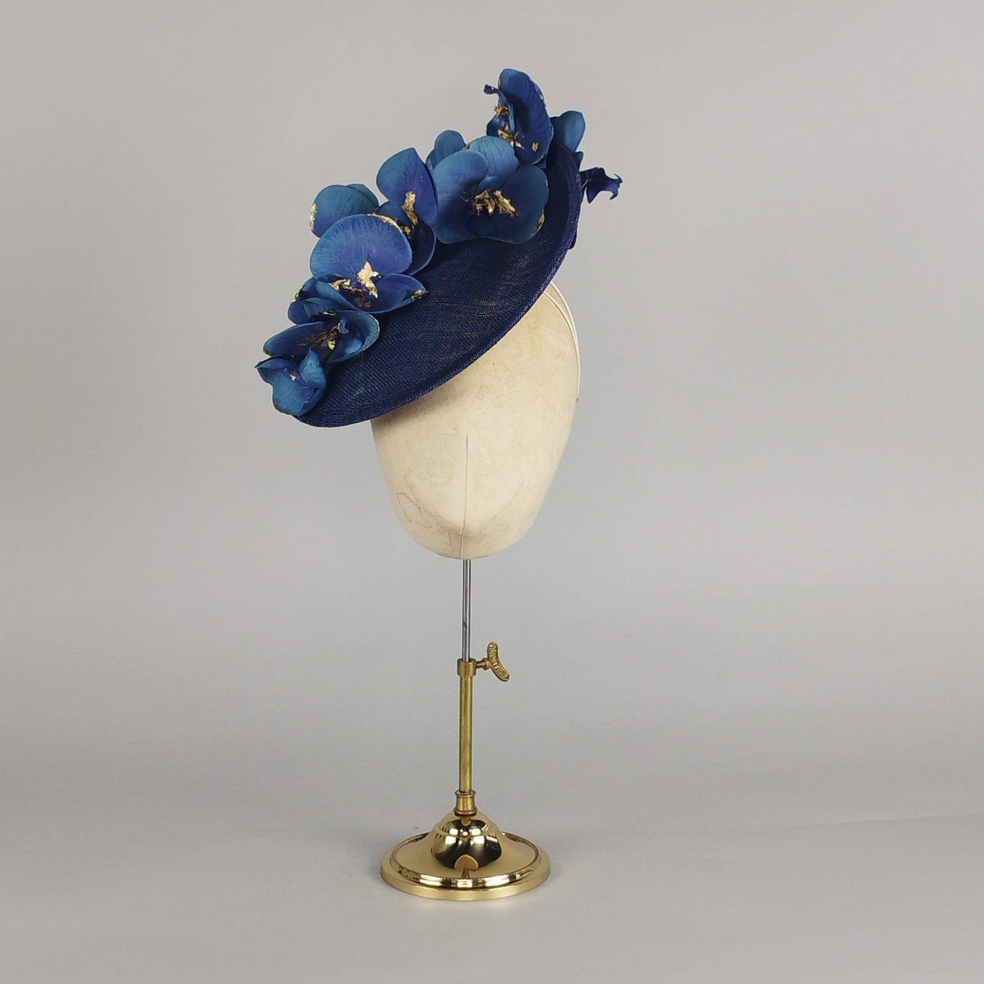 Navy saucer hat adorned with midnight blue orchids and gold leaf, perfect for weddings, Ascot, or luxurious occasions.